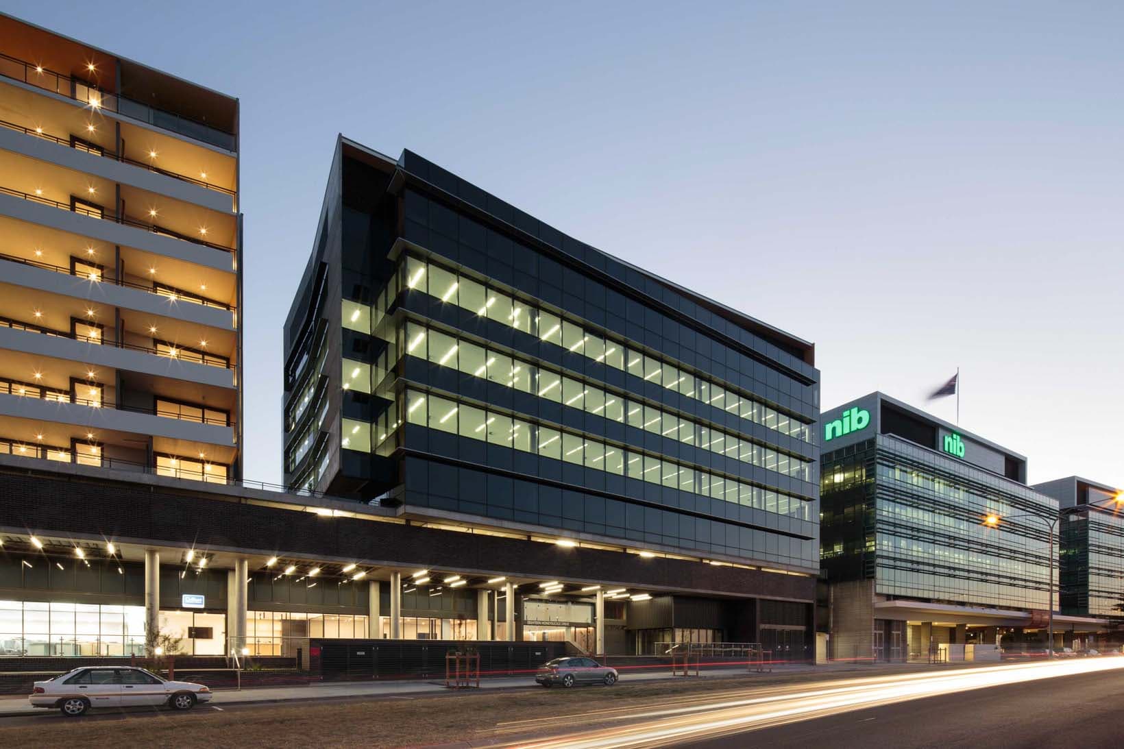 The commercial building viewed from Honeysuckle Drive at dusk, dark glass facade with the residential tower edge visible at left