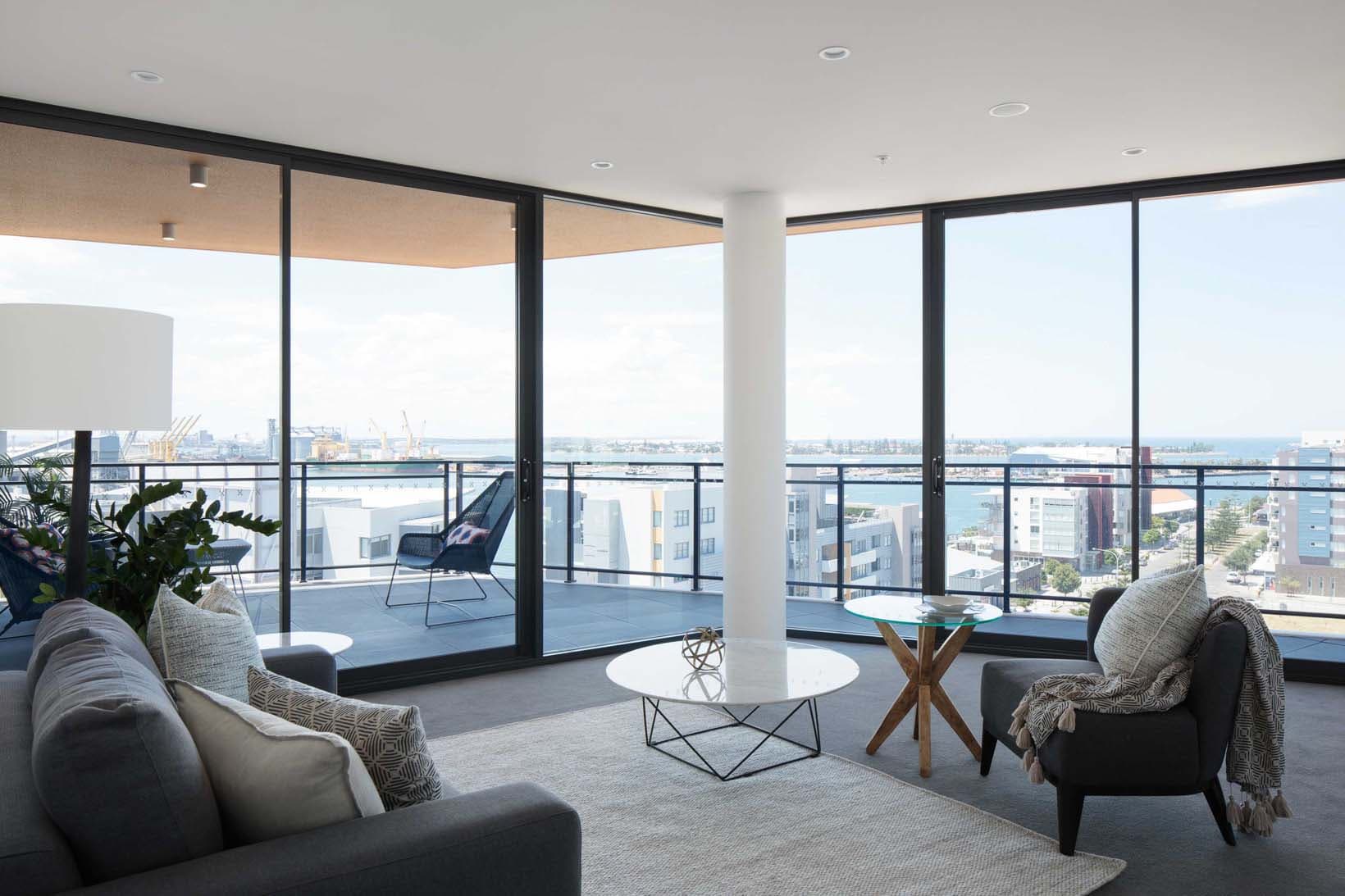 Interior apartment living room with harbour views, floor-to-ceiling glazing opening to a corner balcony overlooking Newcastle Harbour